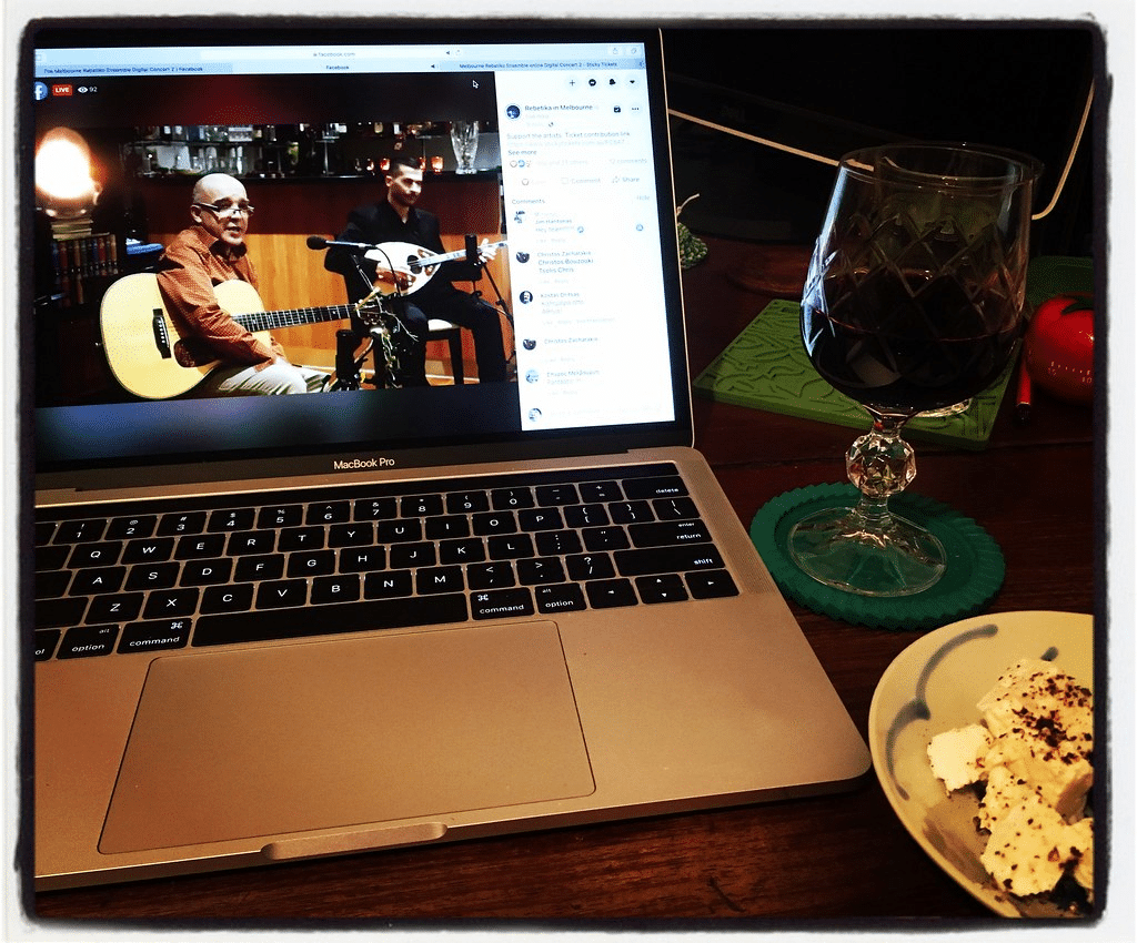 A laptop showing two musicians performing on Facebook Live sits next to food and drink due to COVID-19.