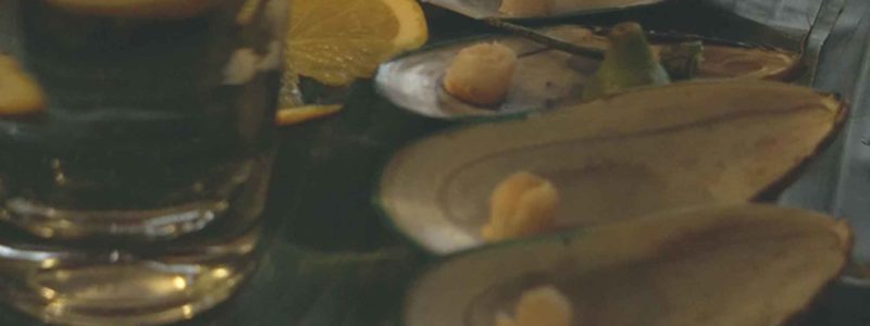 Mussel shells, a lemon wedge and a full glass on a table top.